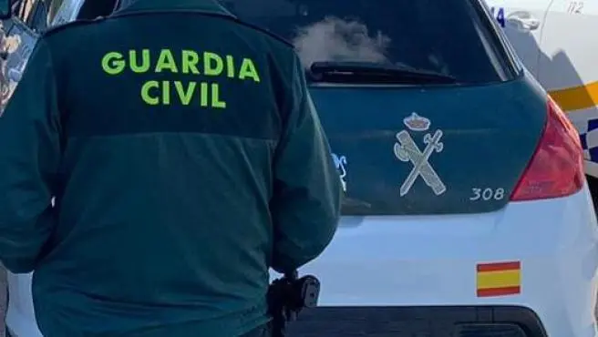 un agente de la guardia civil de espaldas y junto a un vehiculo oficial del cuerpo